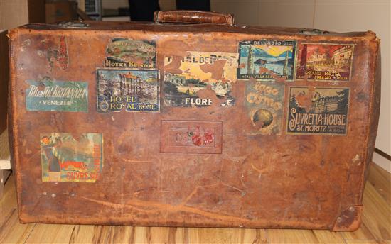 An early 20th century pigskin suitcase, decorated with travel labels, and another suitcase